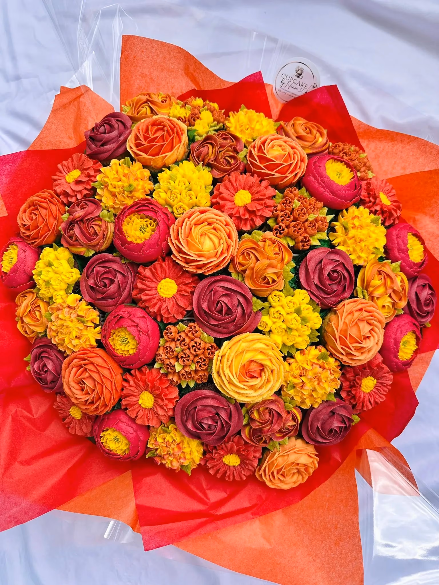 Colorful bouquet of orange, yellow, and red flowers wrapped in red and orange tissue paper.