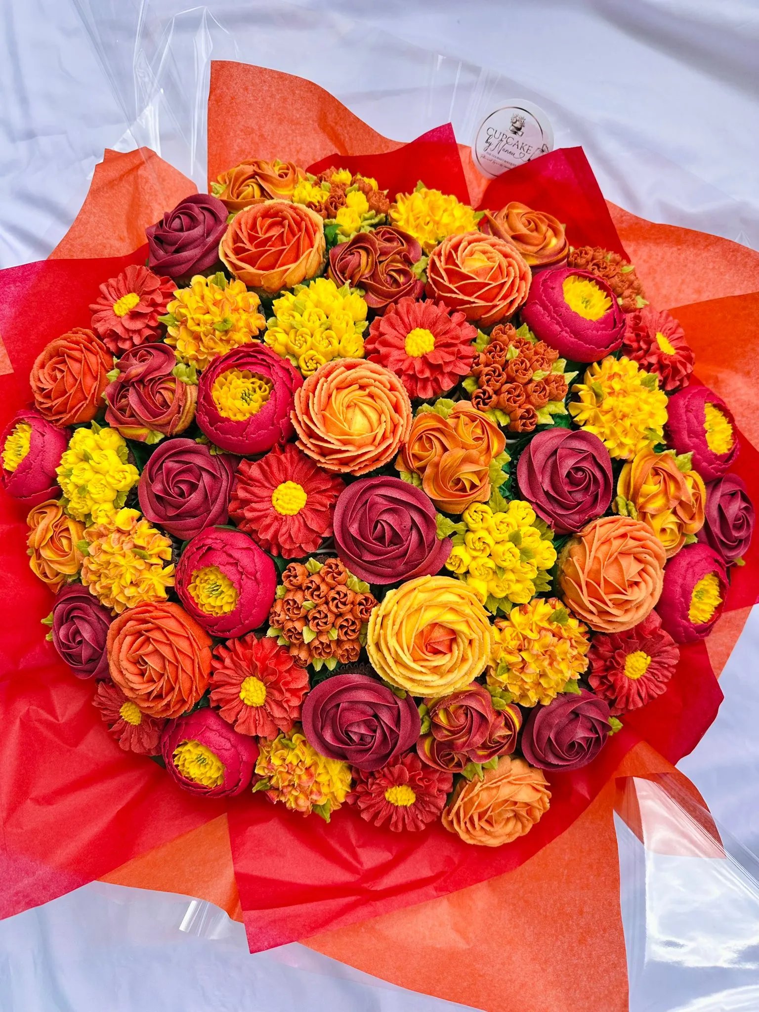 Colorful bouquet of orange, yellow, and red flowers wrapped in red and orange tissue paper.