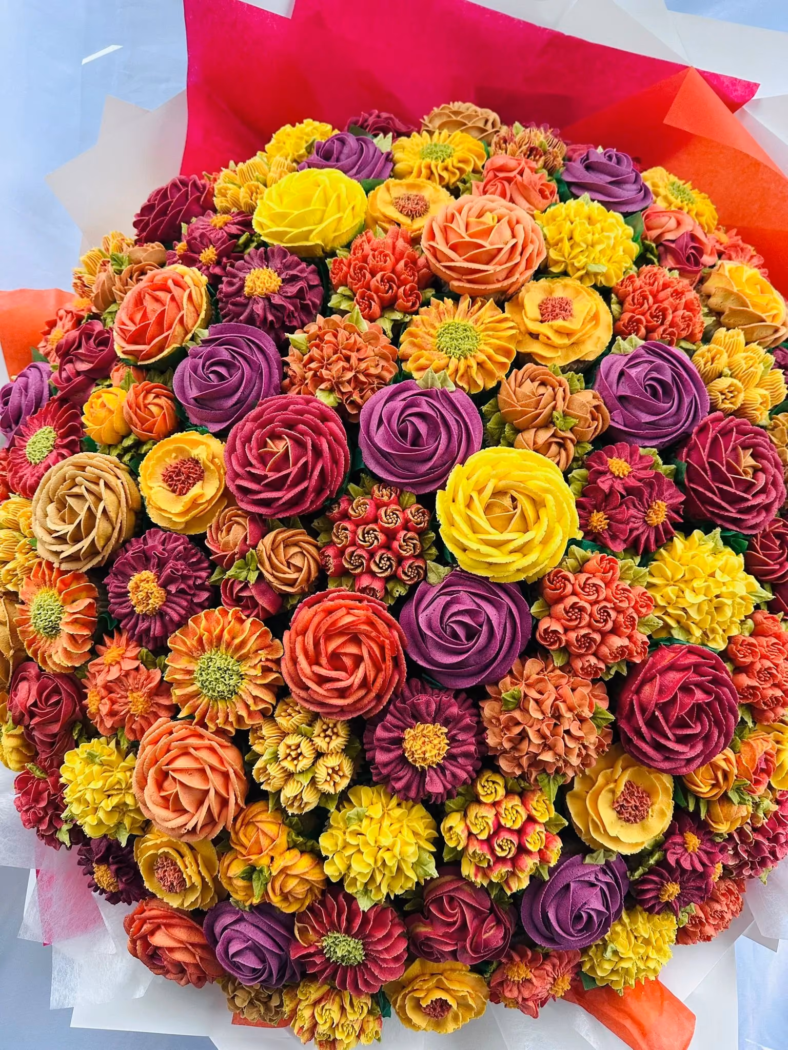 A colorful bouquet of intricately piped buttercream flowers in shades of yellow, orange, purple, and red.