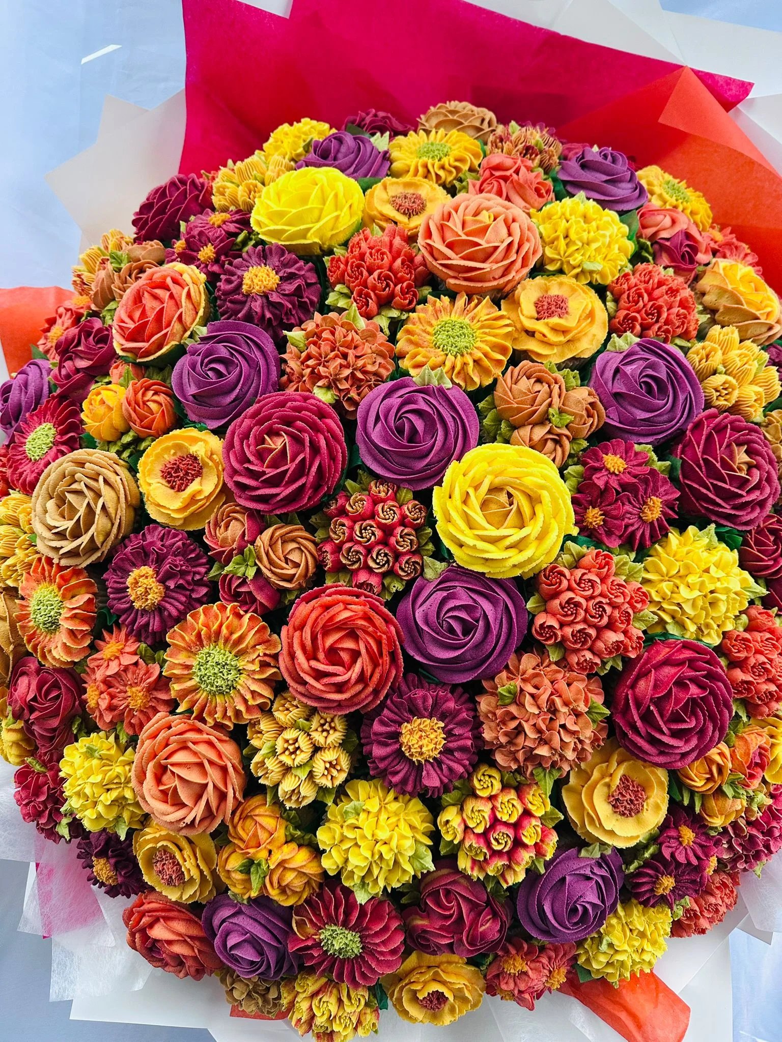 A colorful bouquet of intricately piped buttercream flowers in shades of yellow, orange, purple, and red.