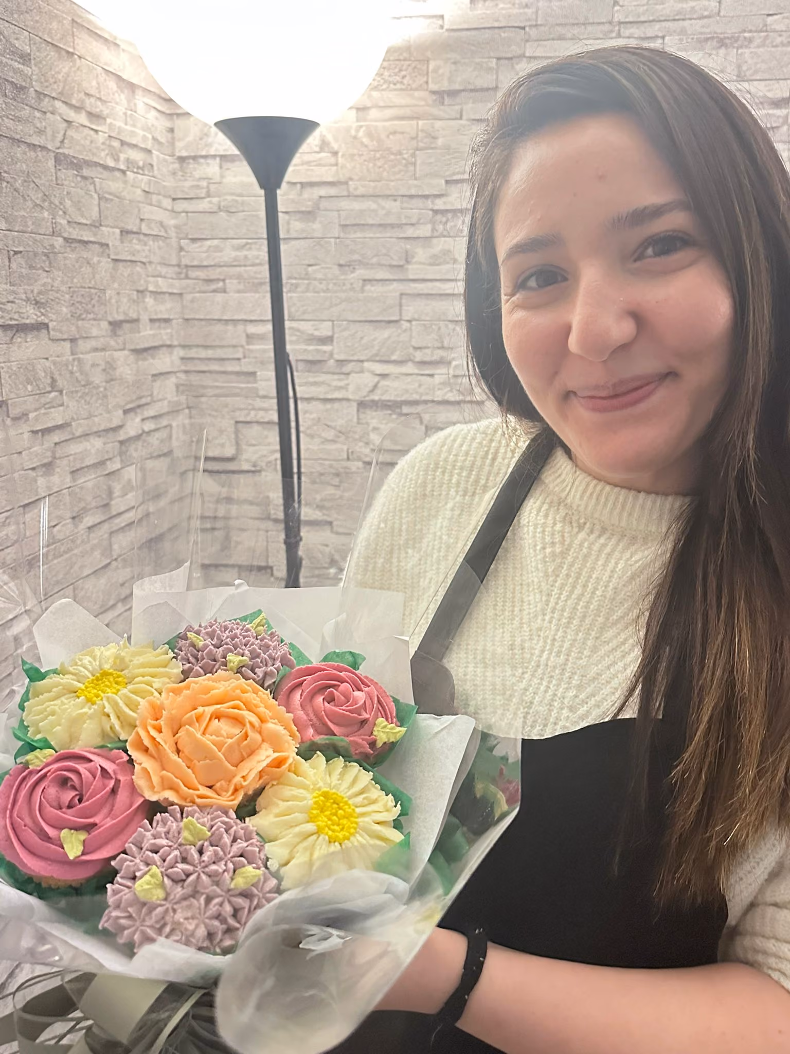 Smiling woman holding a bouquet of colorful flower-shaped cupcakes wrapped in clear plastic.
