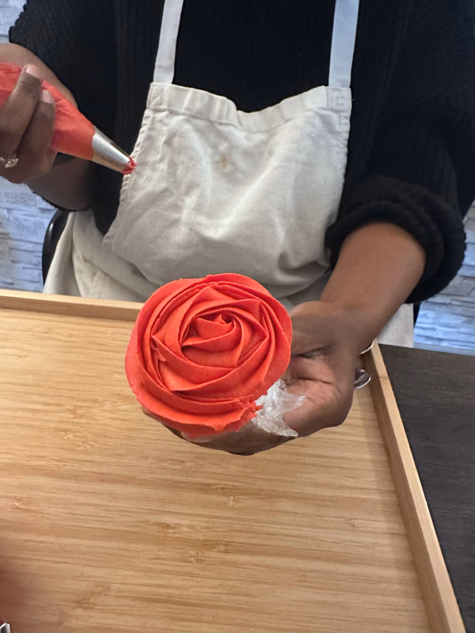 Person holding a piping bag decorating a cupcake with red frosting shaped like a rose.