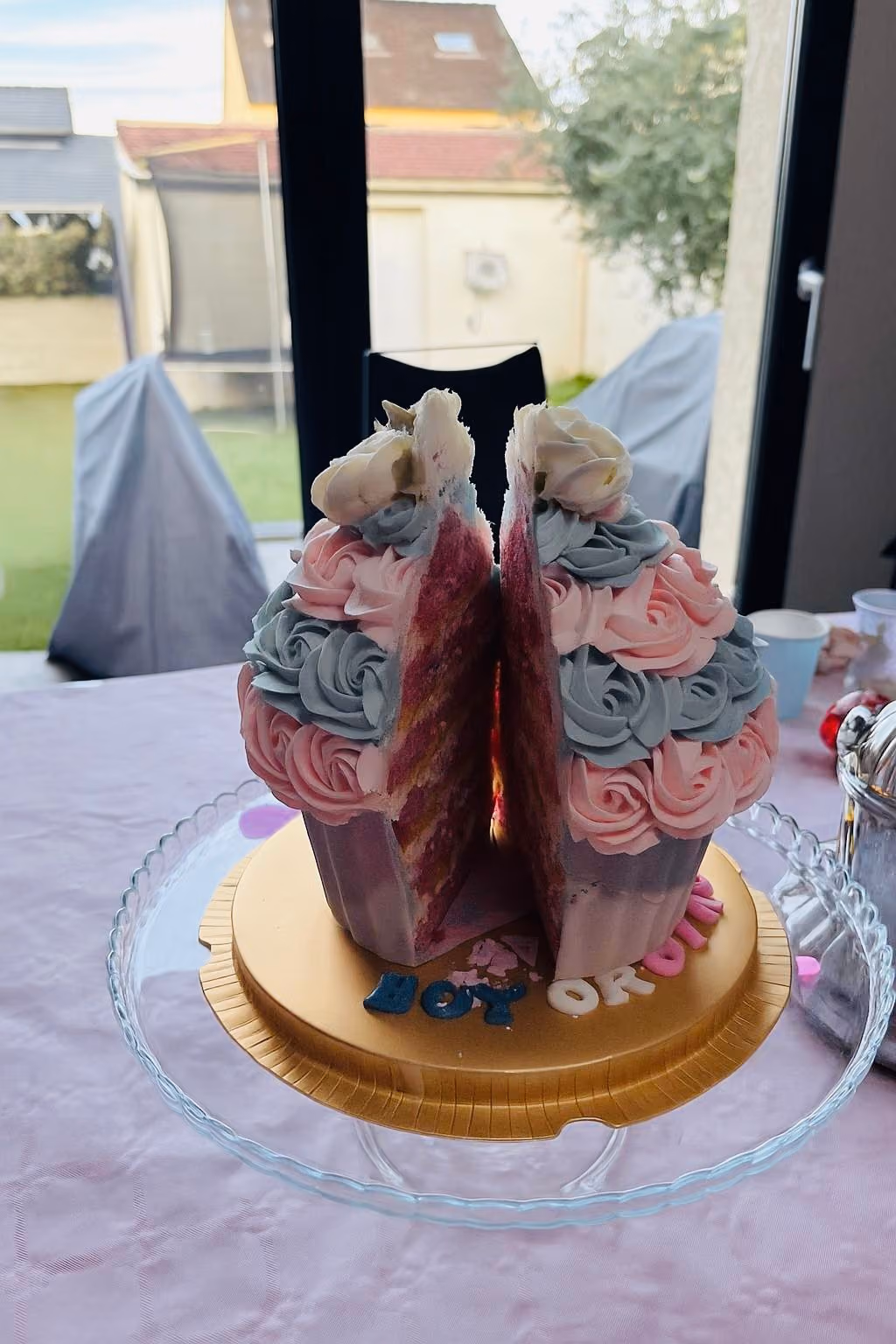 Cut pink and blue gender reveal cake with rosette frosting on a glass cake stand, displaying layered pink and purple interior.