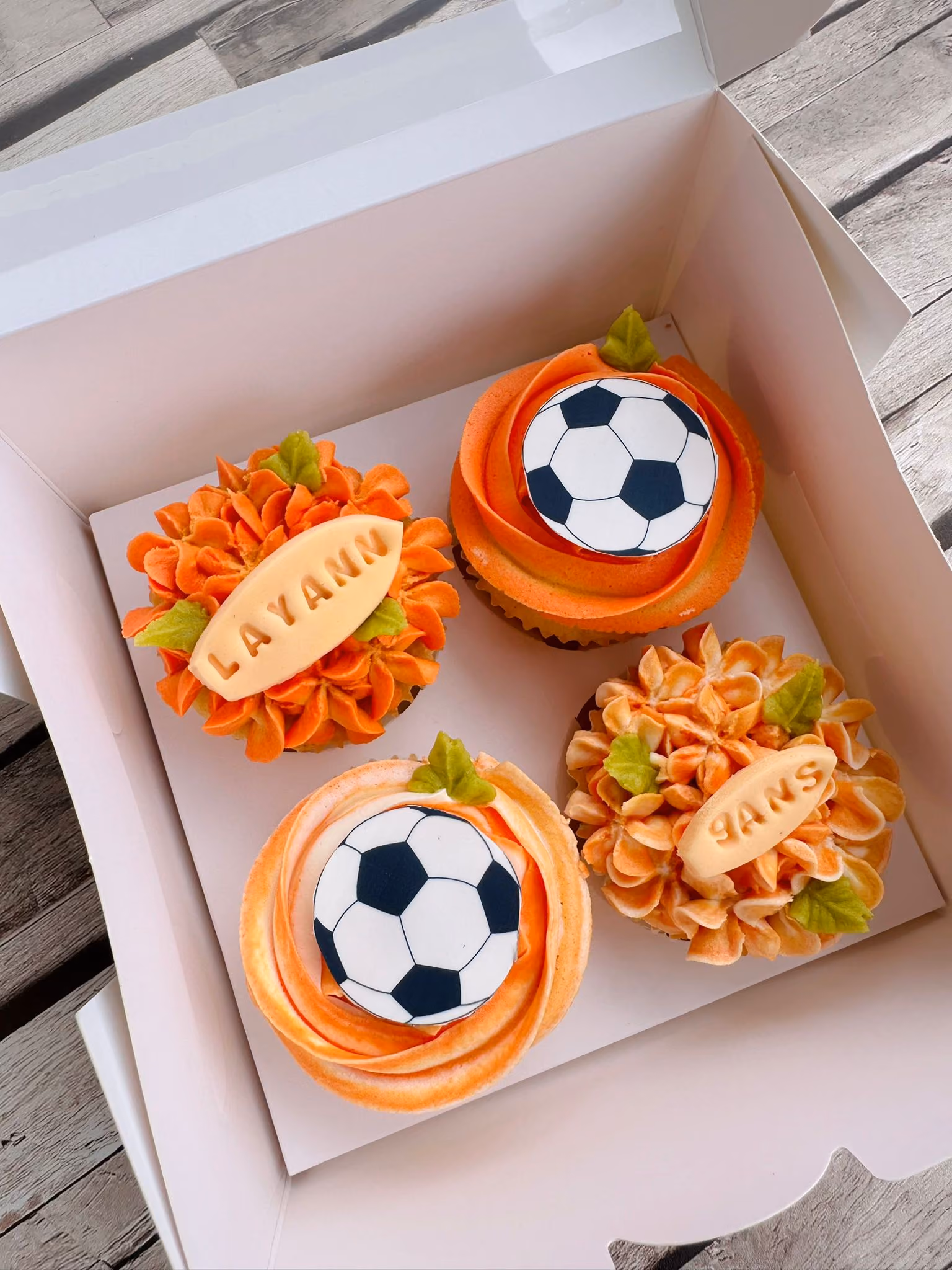 Box of twelve cupcakes decorated with pink, yellow, and red floral buttercream designs.