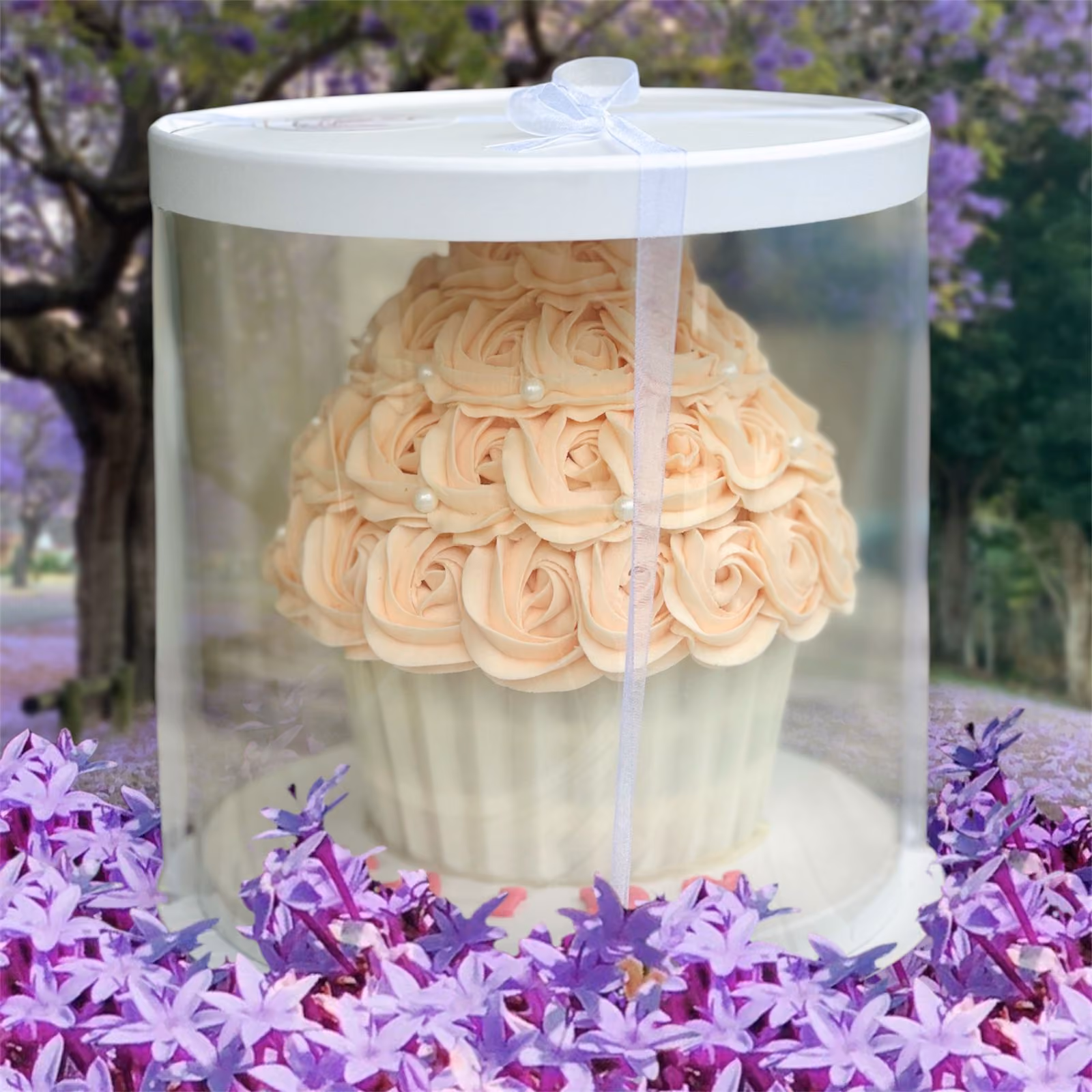 White box containing a dozen cupcakes decorated with intricate buttercream flowers in shades of red, pink, and white with green leaves.