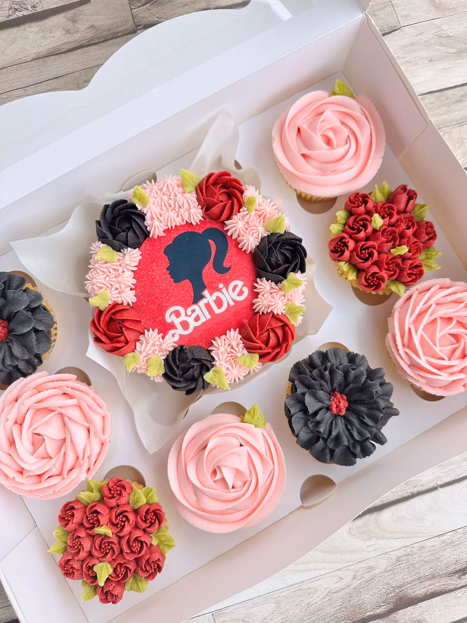 Box of assorted pink and white Hello Kitty-themed cupcakes and a small cake decorated with buttercream flowers.