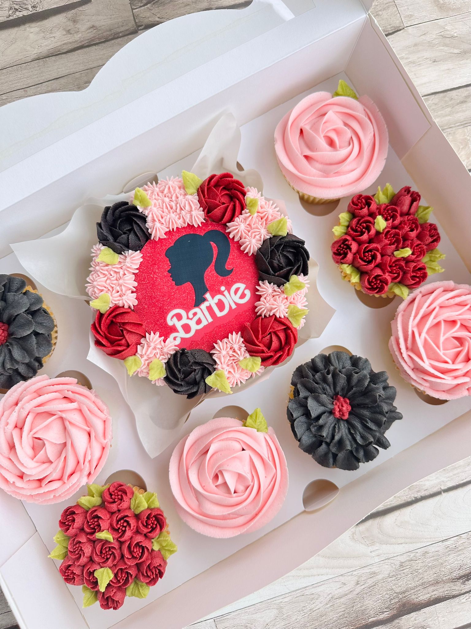 Box of assorted pink and white Hello Kitty-themed cupcakes and a small cake decorated with buttercream flowers.