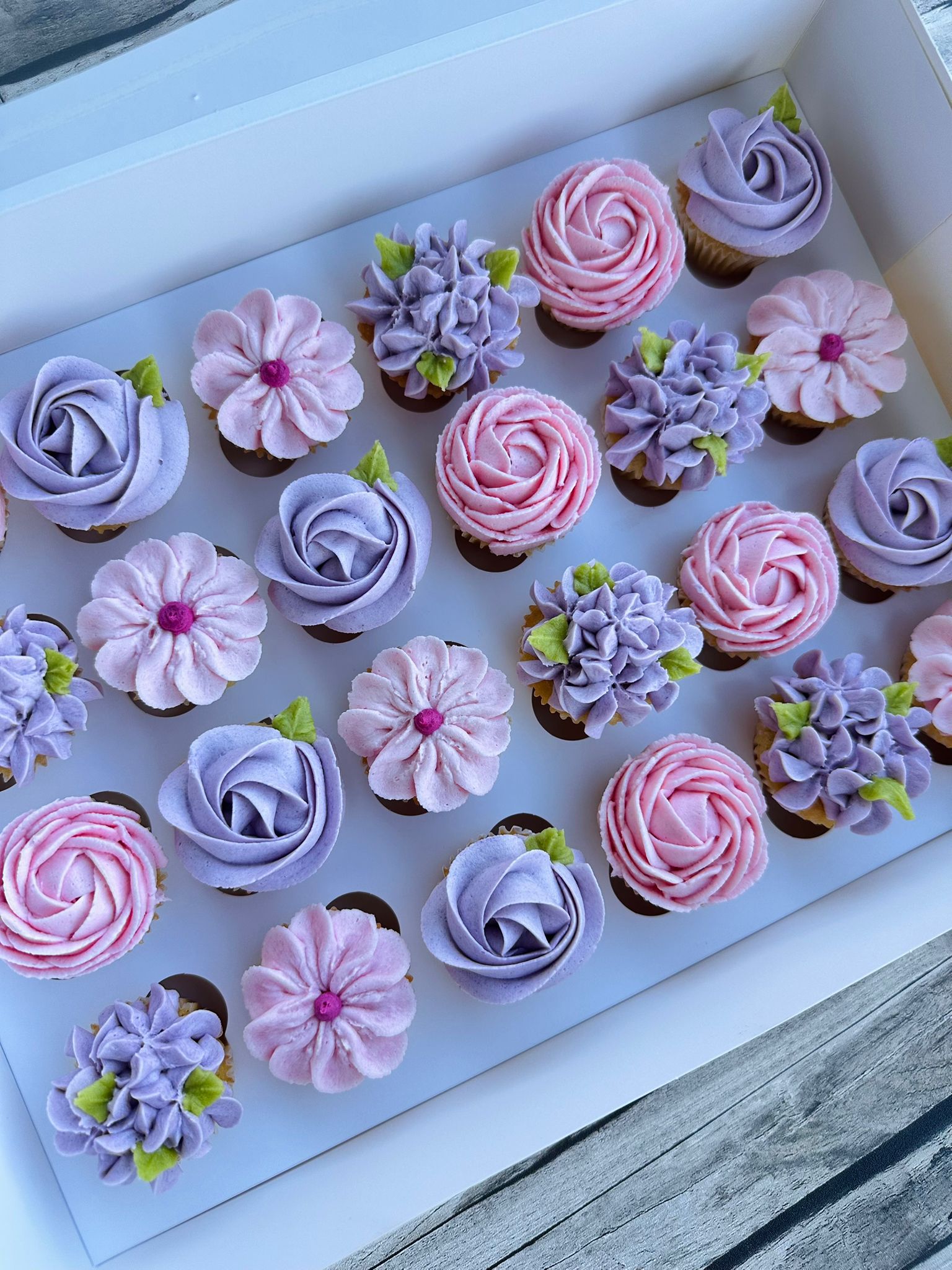 Box of twelve cupcakes decorated with red, orange, and yellow floral frosting designs with green leaves.