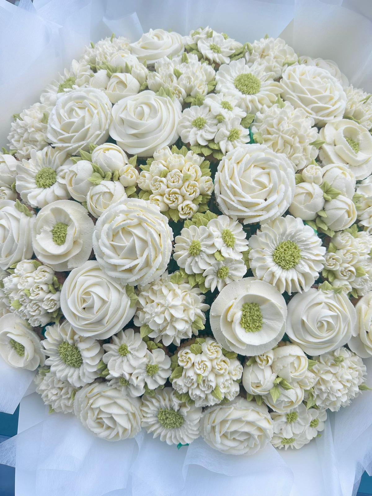 Bouquet of cupcakes decorated with yellow and dark gray frosting designed to resemble flowers, wrapped in yellow paper with a green ribbon.
