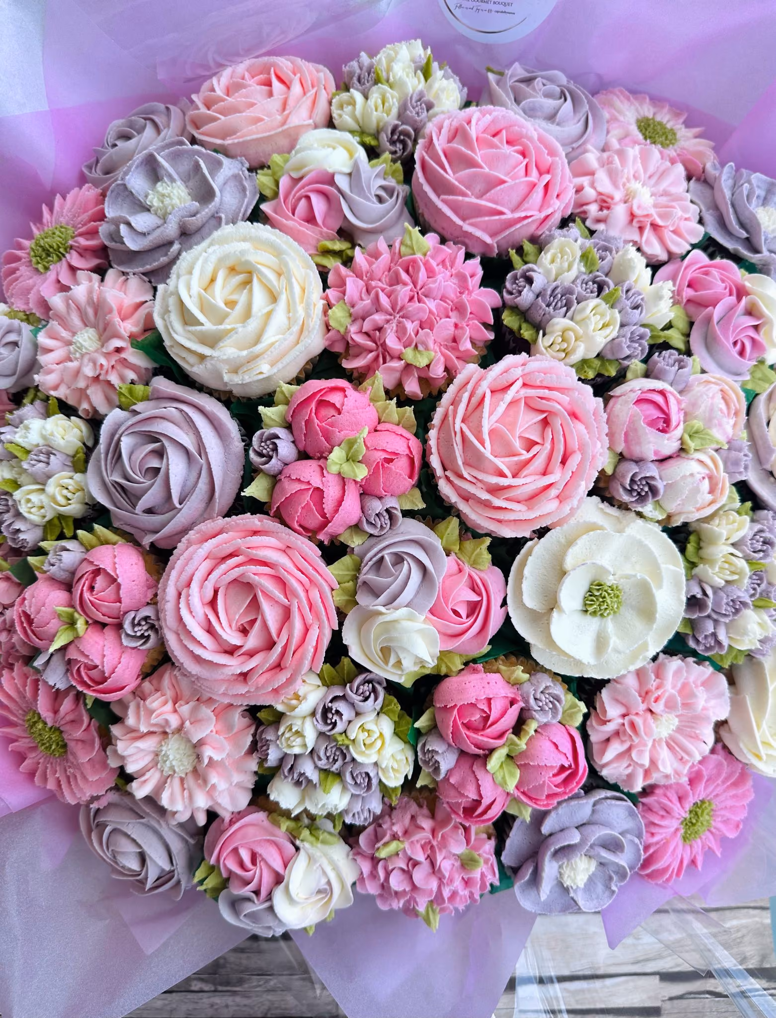 Box of assorted cupcakes decorated with pink, yellow, and green floral buttercream designs.