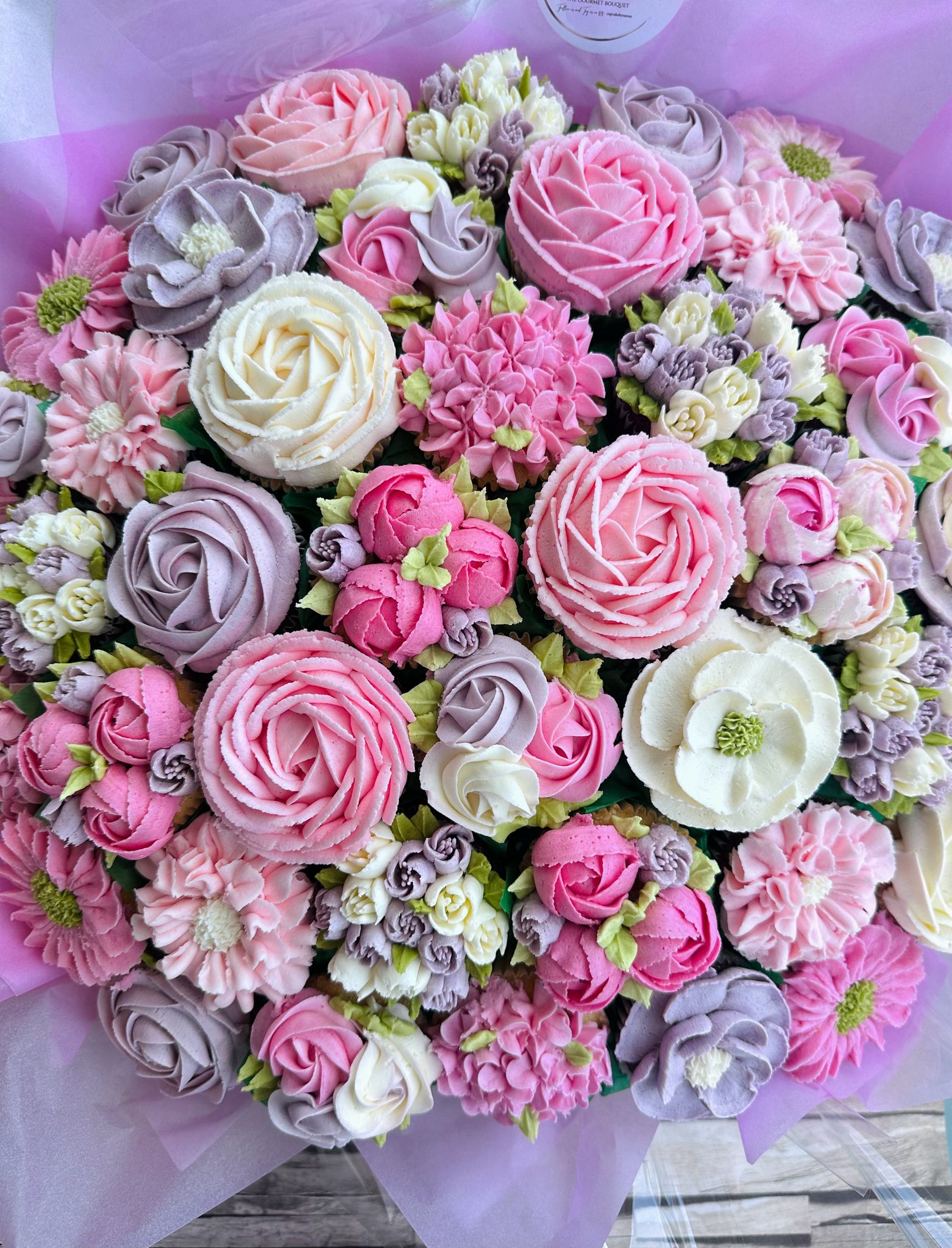 Box of assorted cupcakes decorated with pink, yellow, and green floral buttercream designs.