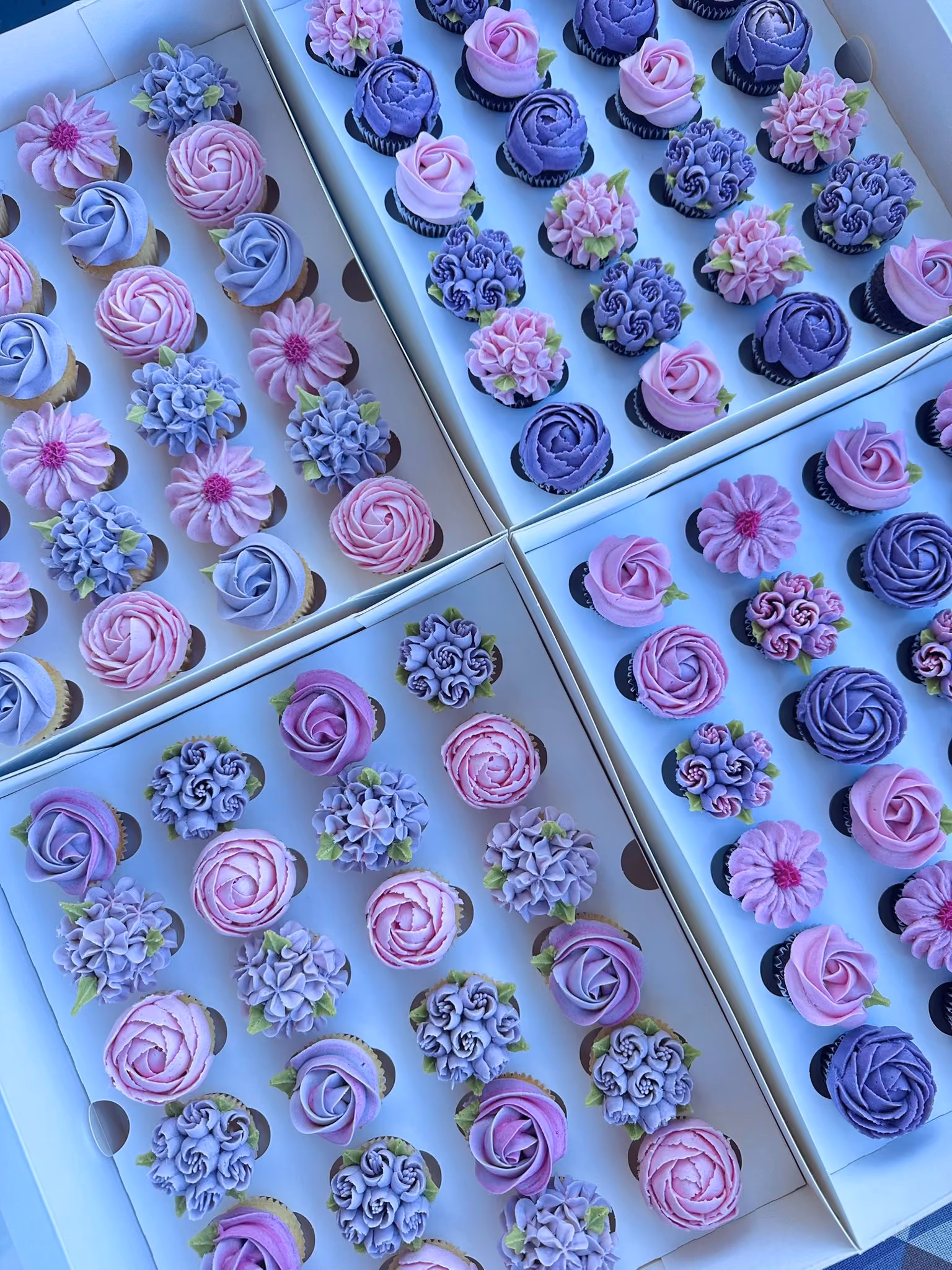 Box of twelve cupcakes decorated with red, orange, and yellow buttercream flowers with green leaves.