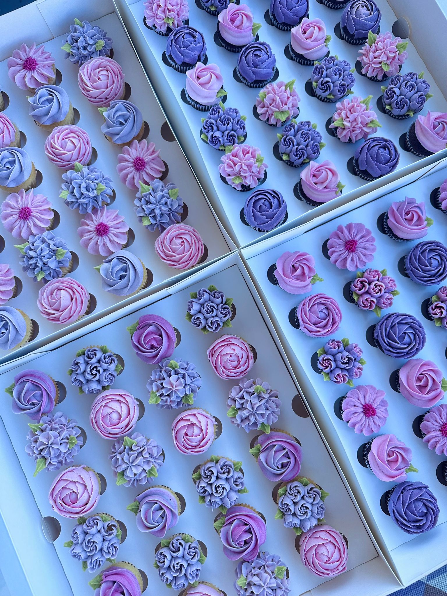 Box of twelve cupcakes decorated with red, orange, and yellow buttercream flowers with green leaves.