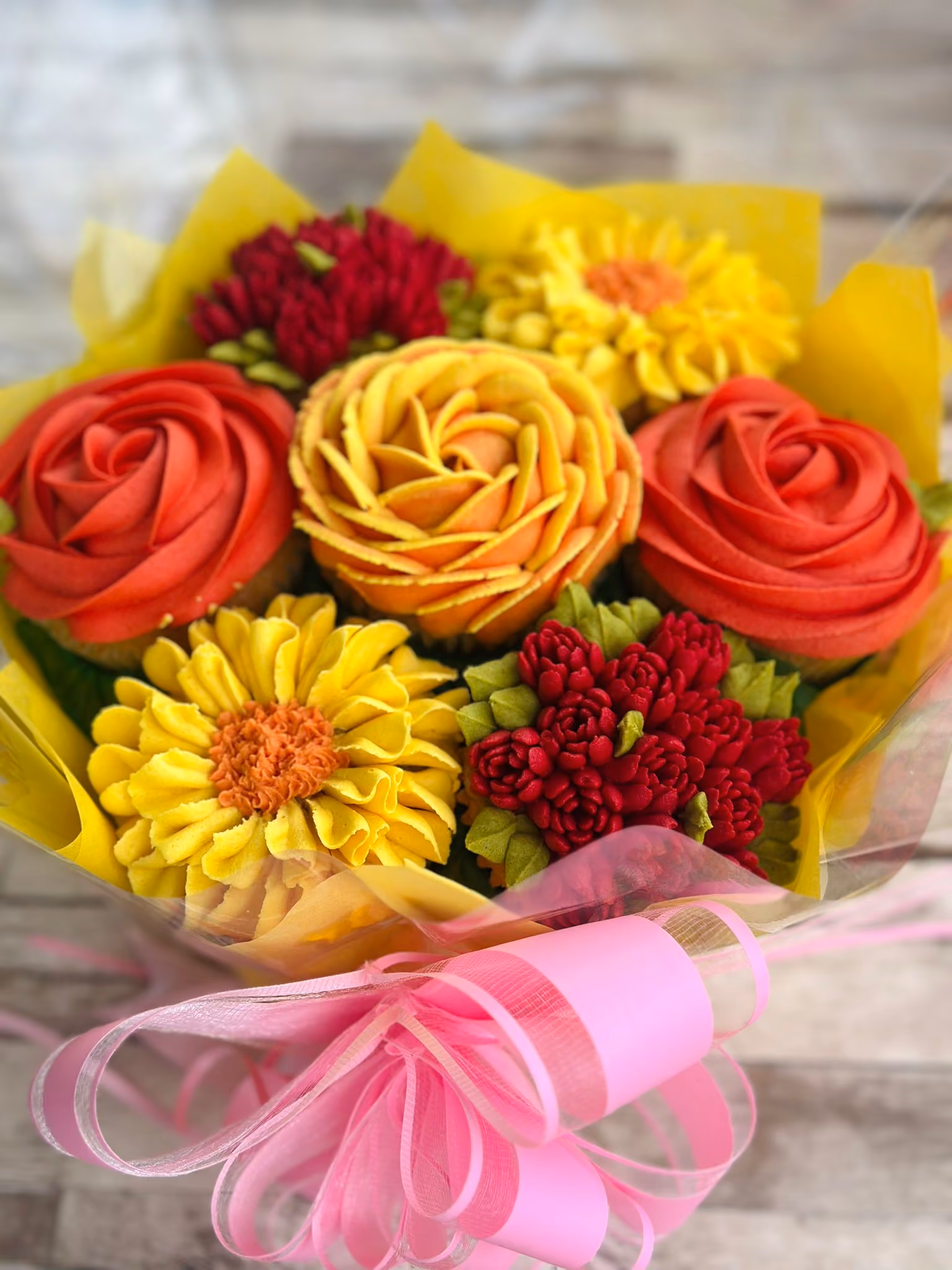 Bouquet of cupcakes decorated with yellow and dark gray frosting designed to resemble flowers, wrapped in yellow paper with a green ribbon.