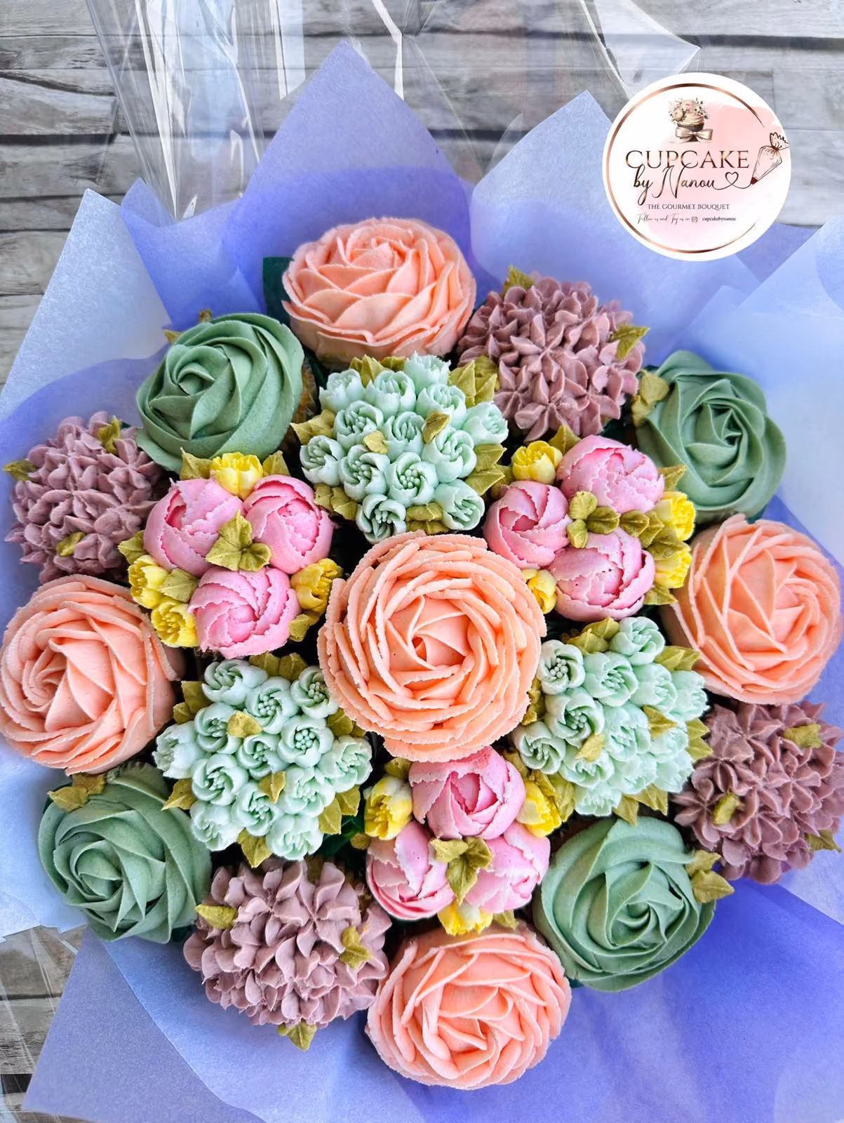 Bouquet of intricately decorated cupcakes with orange and pink floral frosting and green leaves.