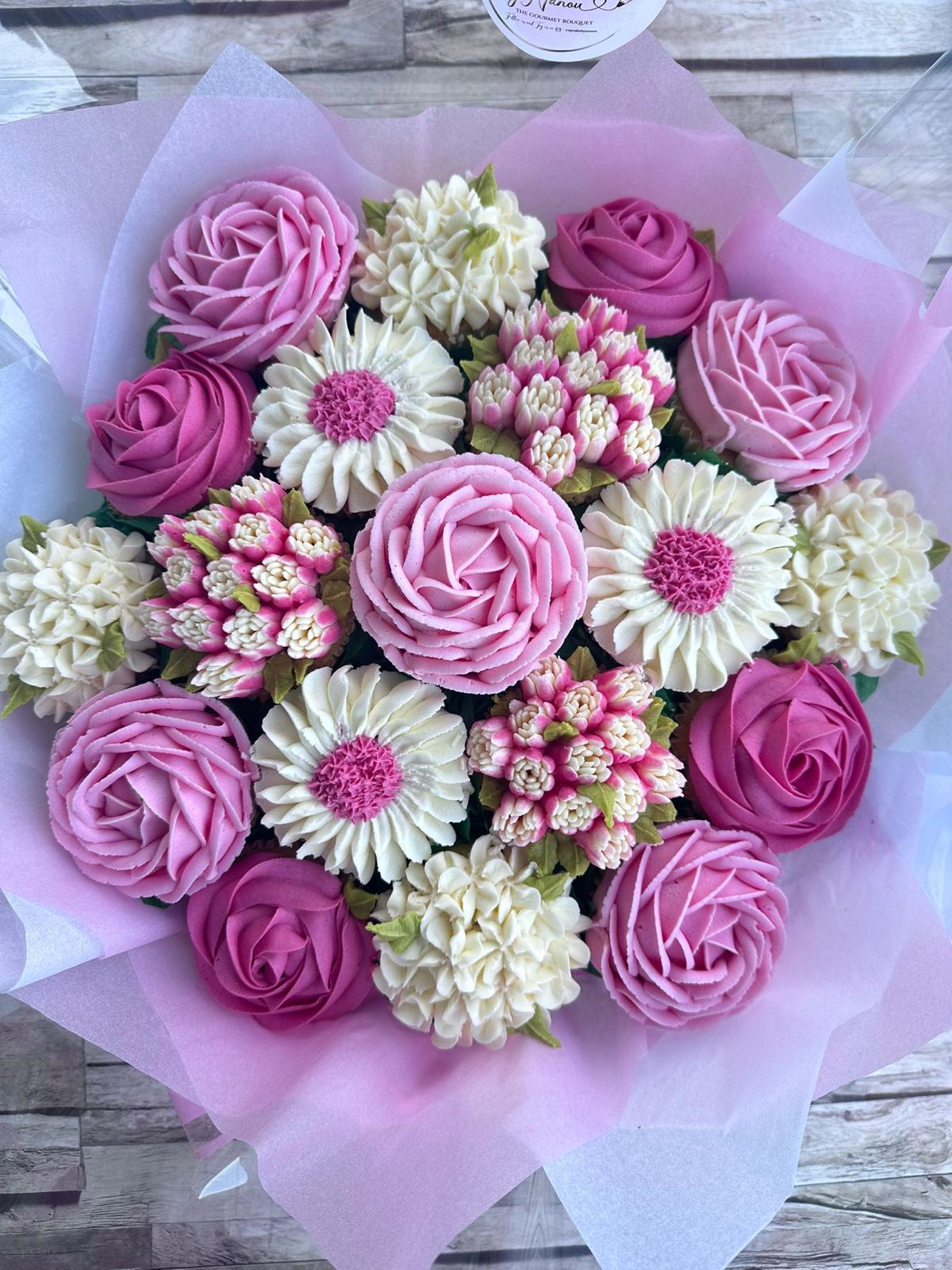 Bouquet of intricately decorated cupcakes with pink and cream floral icing arranged on light purple tissue paper.
