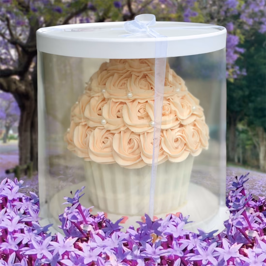 Giant cupcake aux roses pêche dans sa boîte transparente, au milieu de fleurs violettes