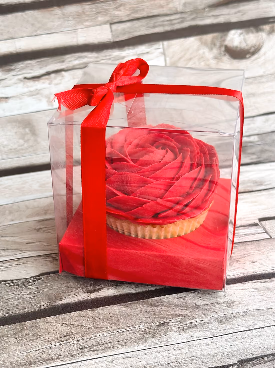 Cupcake rose rouge dans sa boîte cadeau transparente nouée d'un ruban rouge