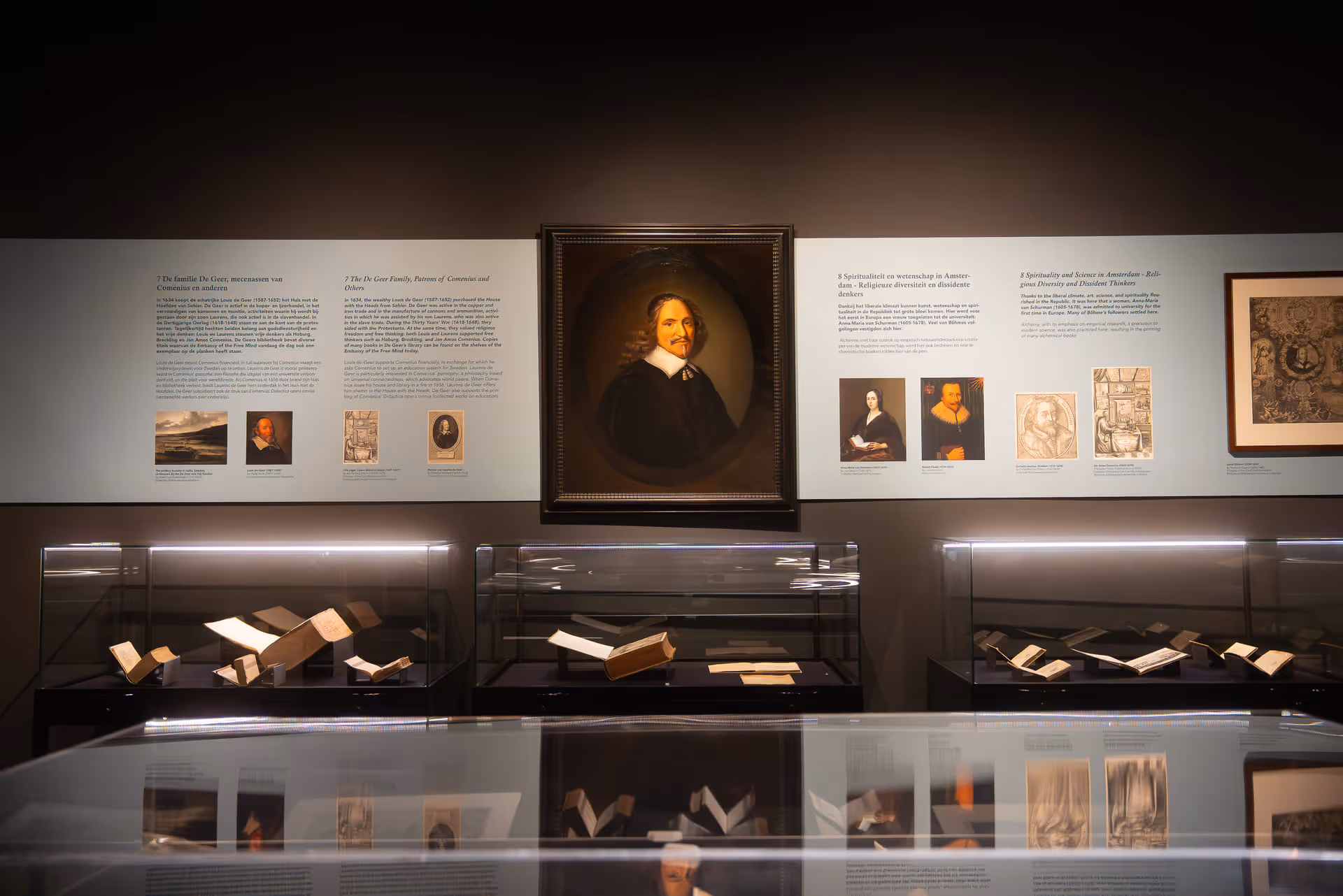 Museum exhibit with a framed portrait of a man in historical attire above glass cases displaying old books and documents.