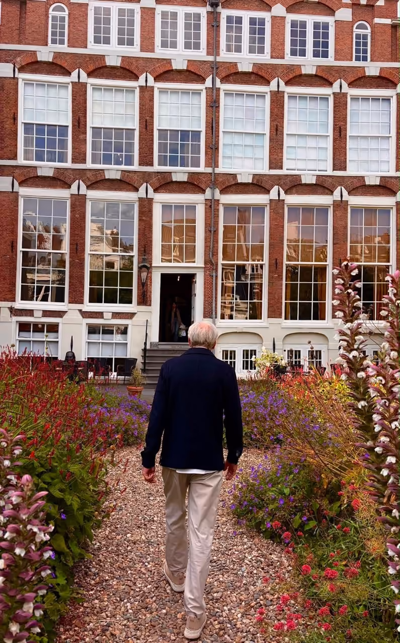 Jons Hensel in the garden of The Embassy of the Free Mind, facing away and walking toward our museum building.