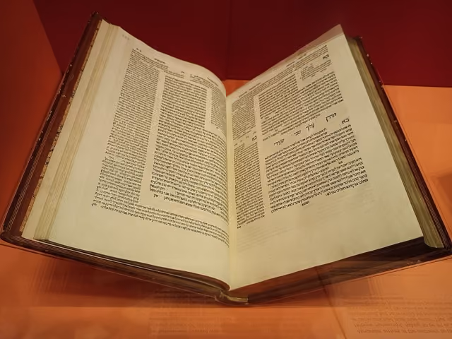 An open 1520s Bomberg Talmud book displaying columns of printed Hebrew text under soft lighting on a warm wooden table.