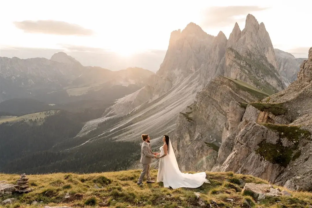 Hochzeitspaar hält sich auf einem grasbewachsenen Berg mit markanten Felsen und Sonnenuntergang fest.