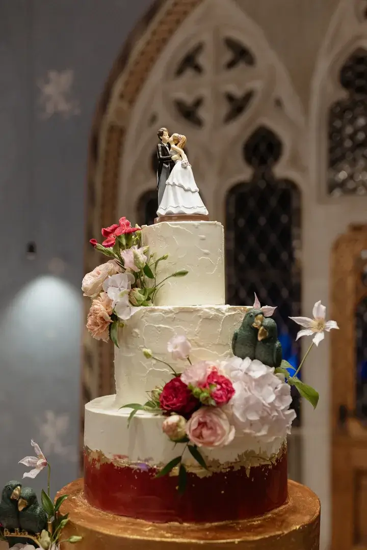 Mehrstöckige Hochzeitstorte mit Brautpaar-Figur und Blumen in einer Kirche.