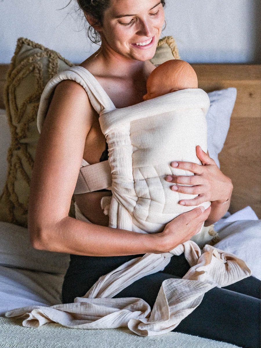A mother holding her baby in the corn husk textile baby carrier concept.