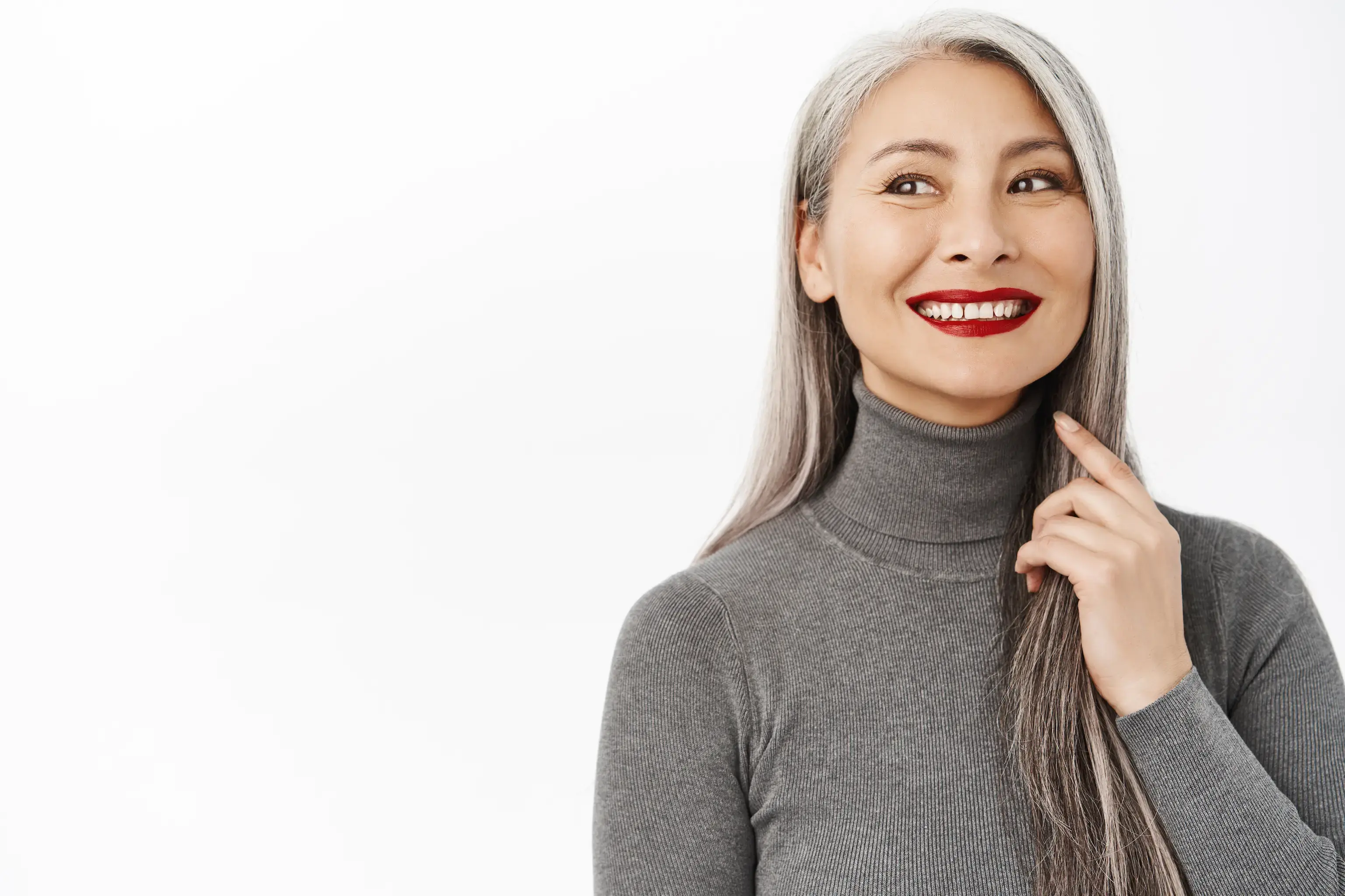 Smiling woman with long gray hair and red lipstick wearing a gray turtleneck sweater against a white background.