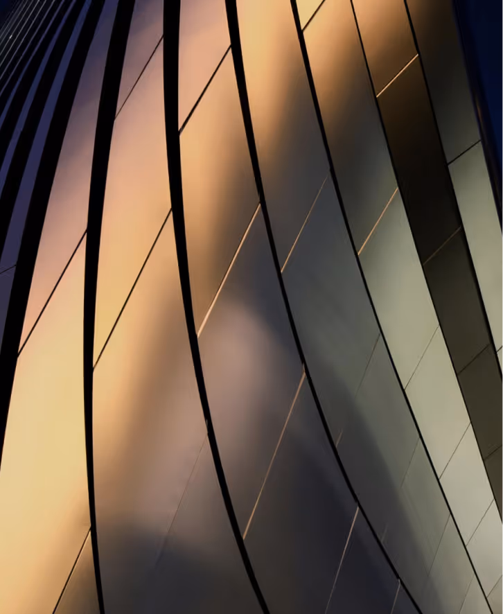 Close-up of a curved modern building facade with reflective glass panels illuminated by warm light.