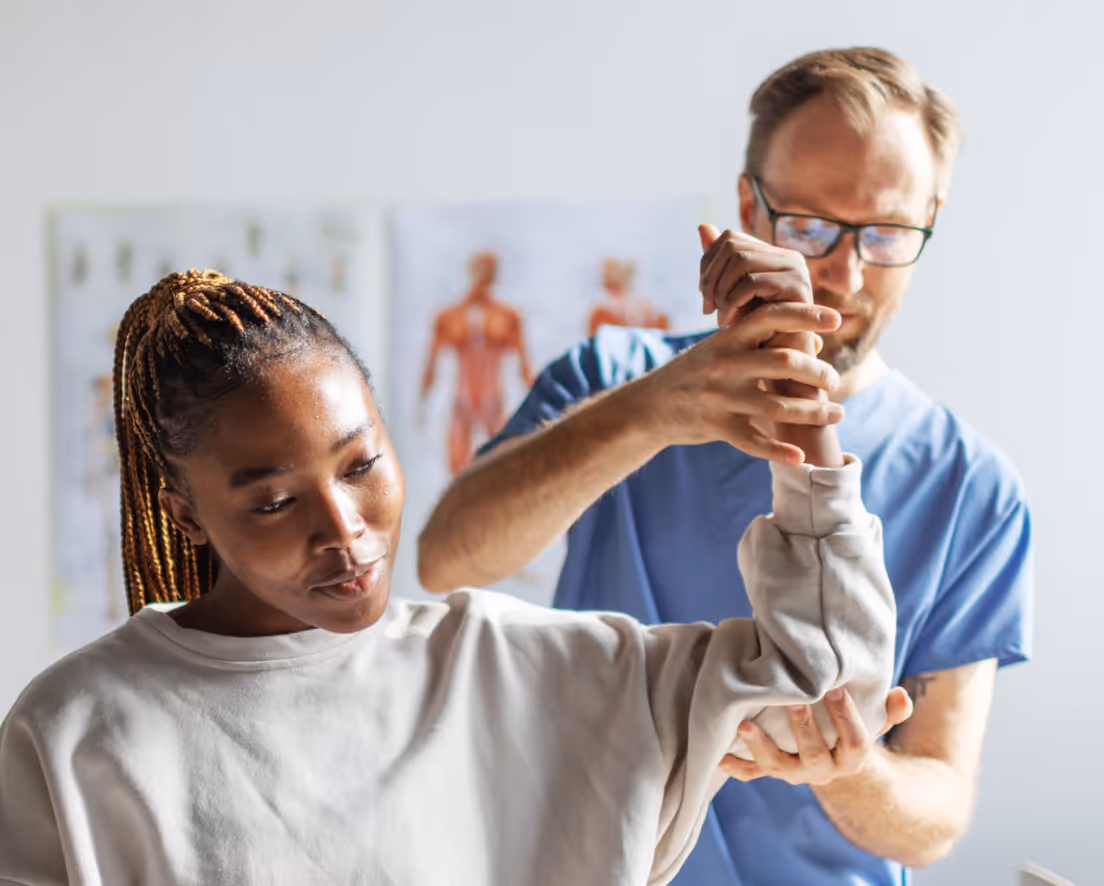 Physical therapist in blue scrubs assisting woman with arm stretch during rehabilitation session.