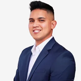 Smiling man in a navy blue suit and white shirt against a plain background.
