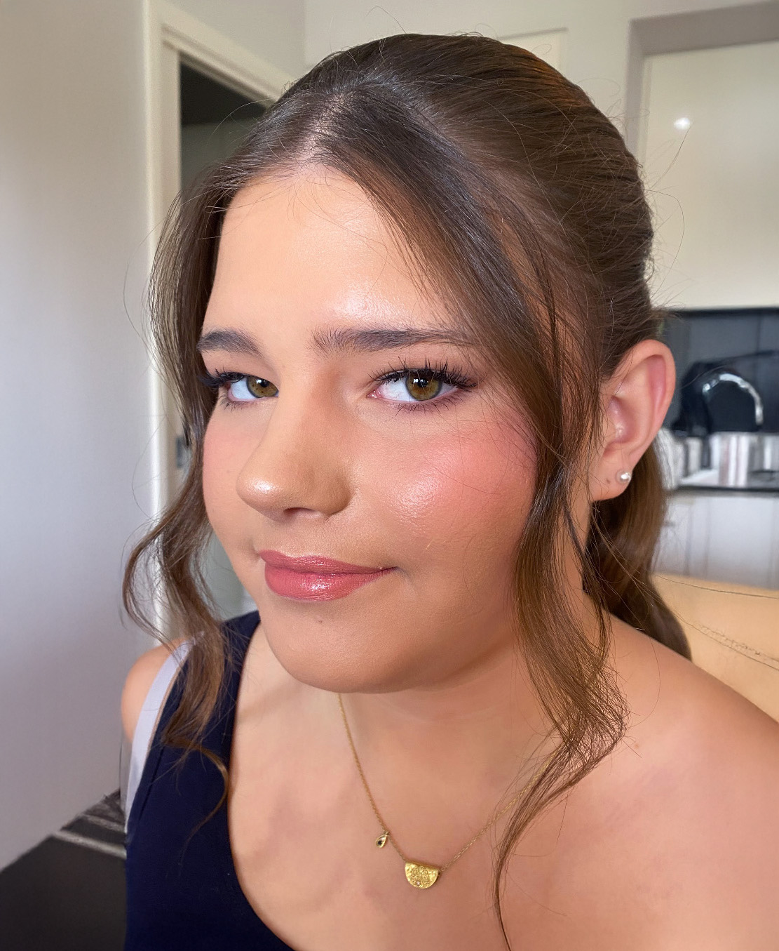 Portrait of a woman with wavy brown hair, bold brown lipstick, and shimmery gold eye makeup wearing an off-shoulder black top.