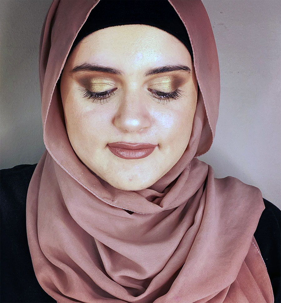 Young woman with colorful rainbow eyeshadow and glossy lips holding a container of makeup brushes.