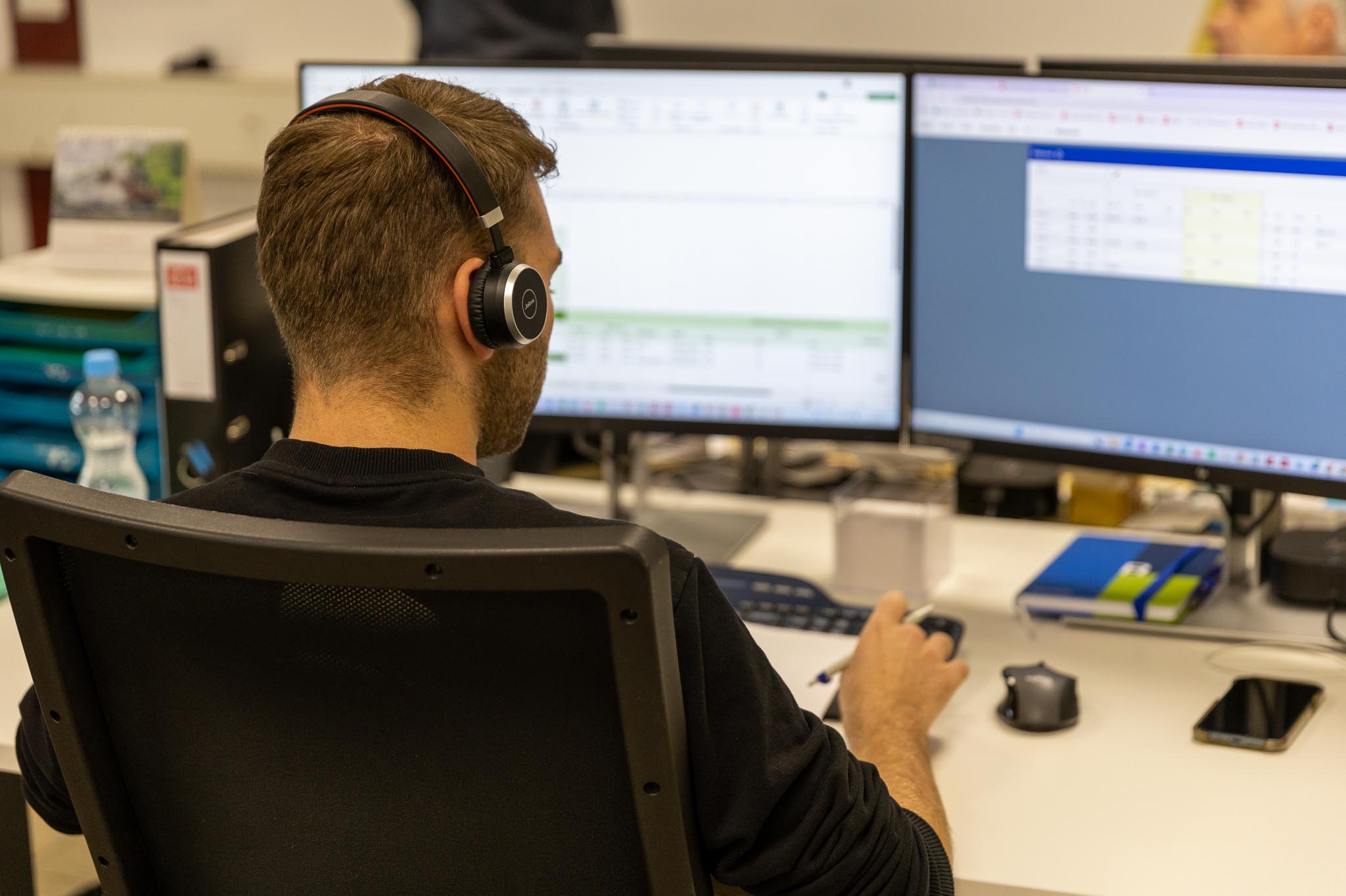 Mann sitzt am Arbeitsplatz mit Headset.