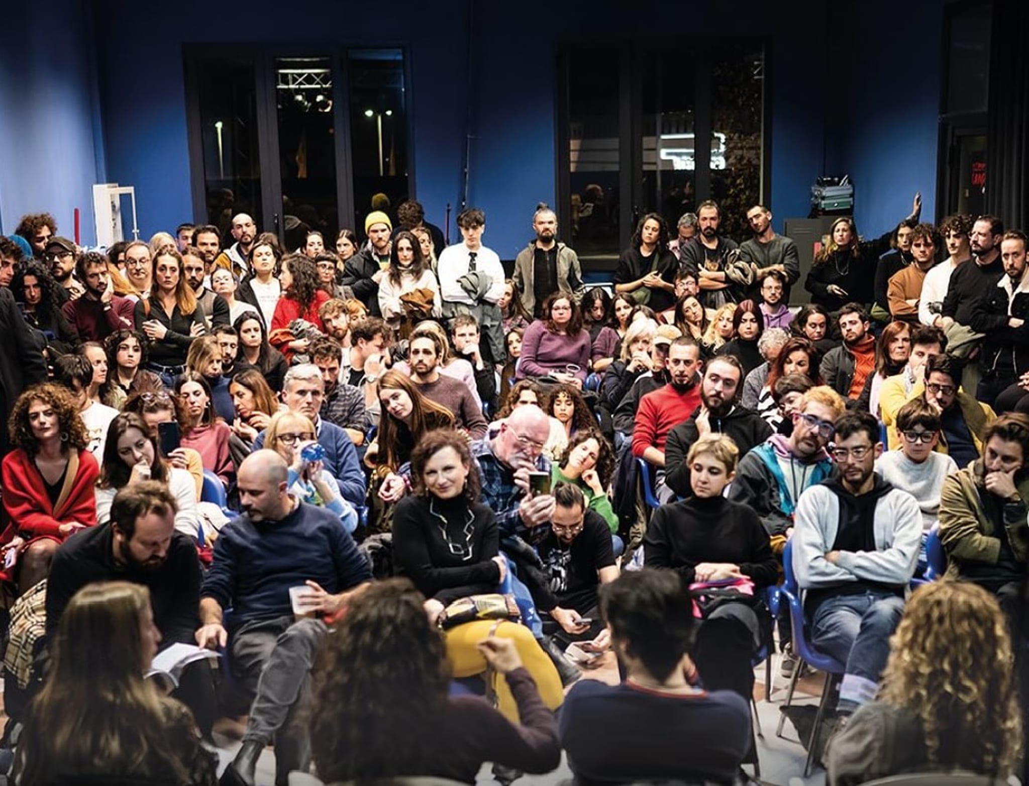 Sala gremita di persone sedute che ascoltano un intervento
