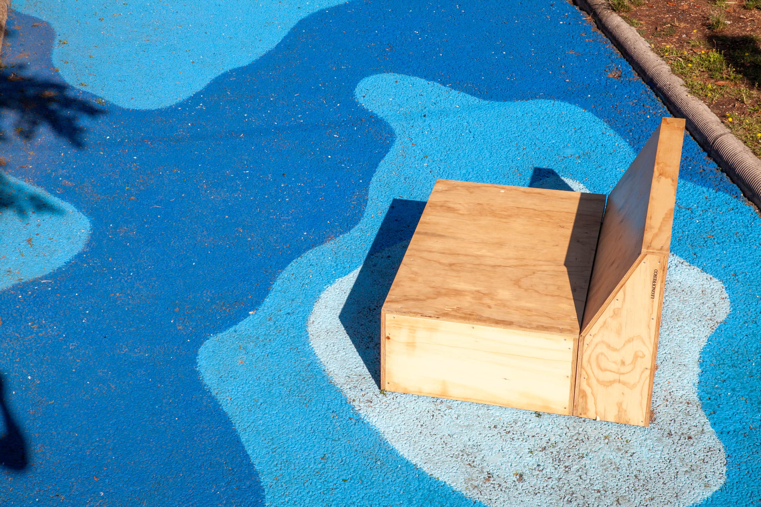 Seduta in legno su una pavimentazione dipinta con forme in diverse tonalità di blu