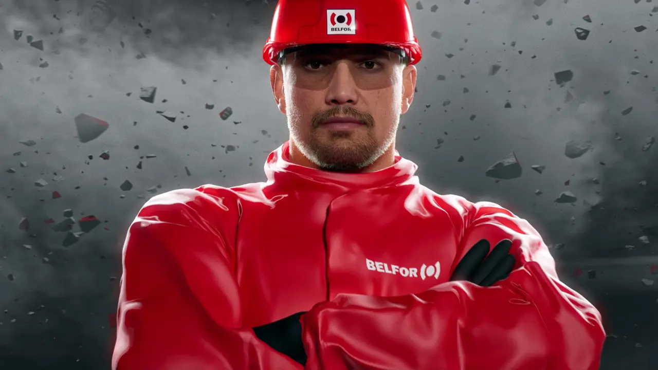 Mann in rotem Schutzhelm und rotem Arbeitsanzug mit verschränkten Armen vor einem Hintergrund aus schwebenden Trümmerstücken.