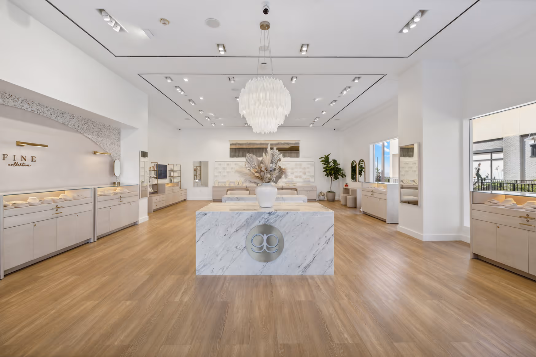 Bright modern jewelry store interior with wooden flooring, marble display table adorned with a flower vase, and multiple glass display cases along the walls.