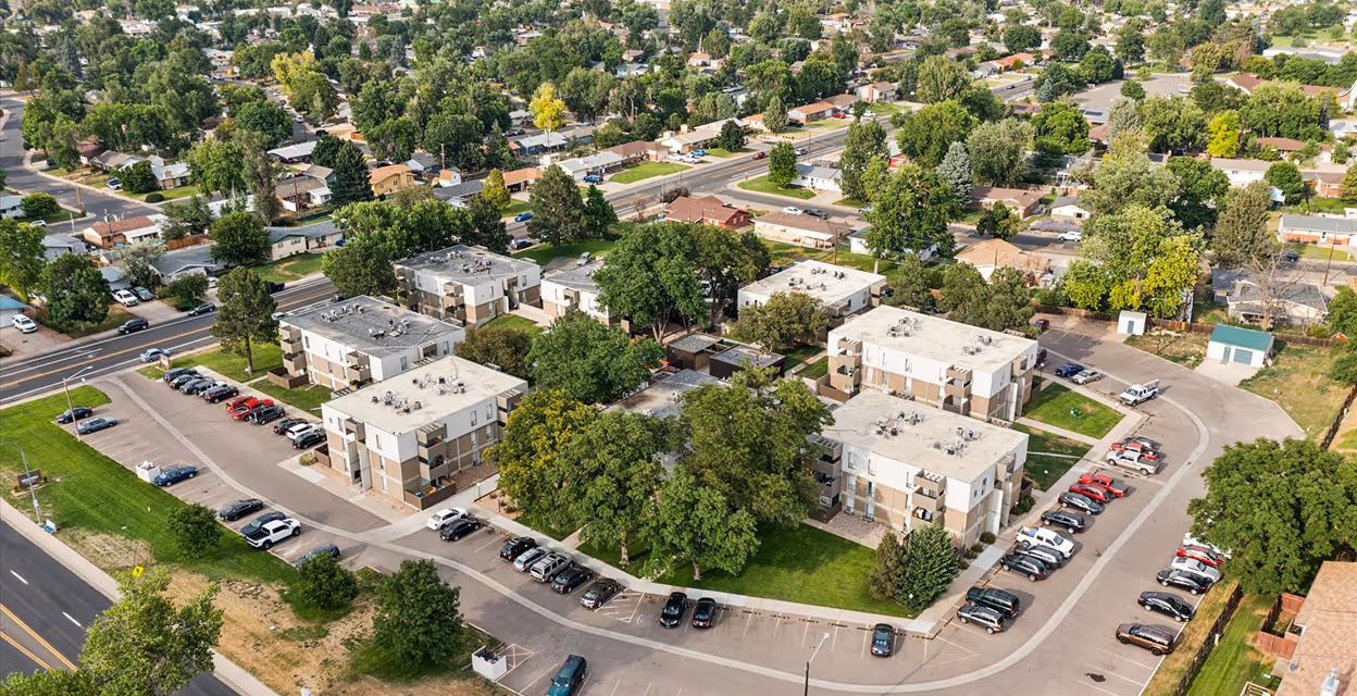 Aerial view of a residential neighborhood showing several low-rise apartment buildings surrounded by trees and parking lots.