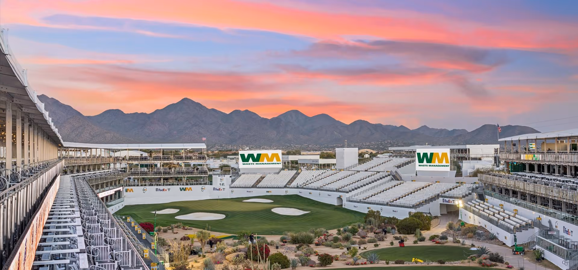 Golf tournament grandstands overlooking a green with sand bunkers at sunset, with mountains in the background and Waste Management branding visible.
