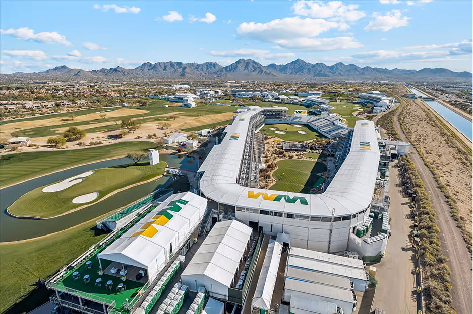 Aerial view of a large golf tournament stadium and course with desert landscape and mountains in the background under a blue sky.