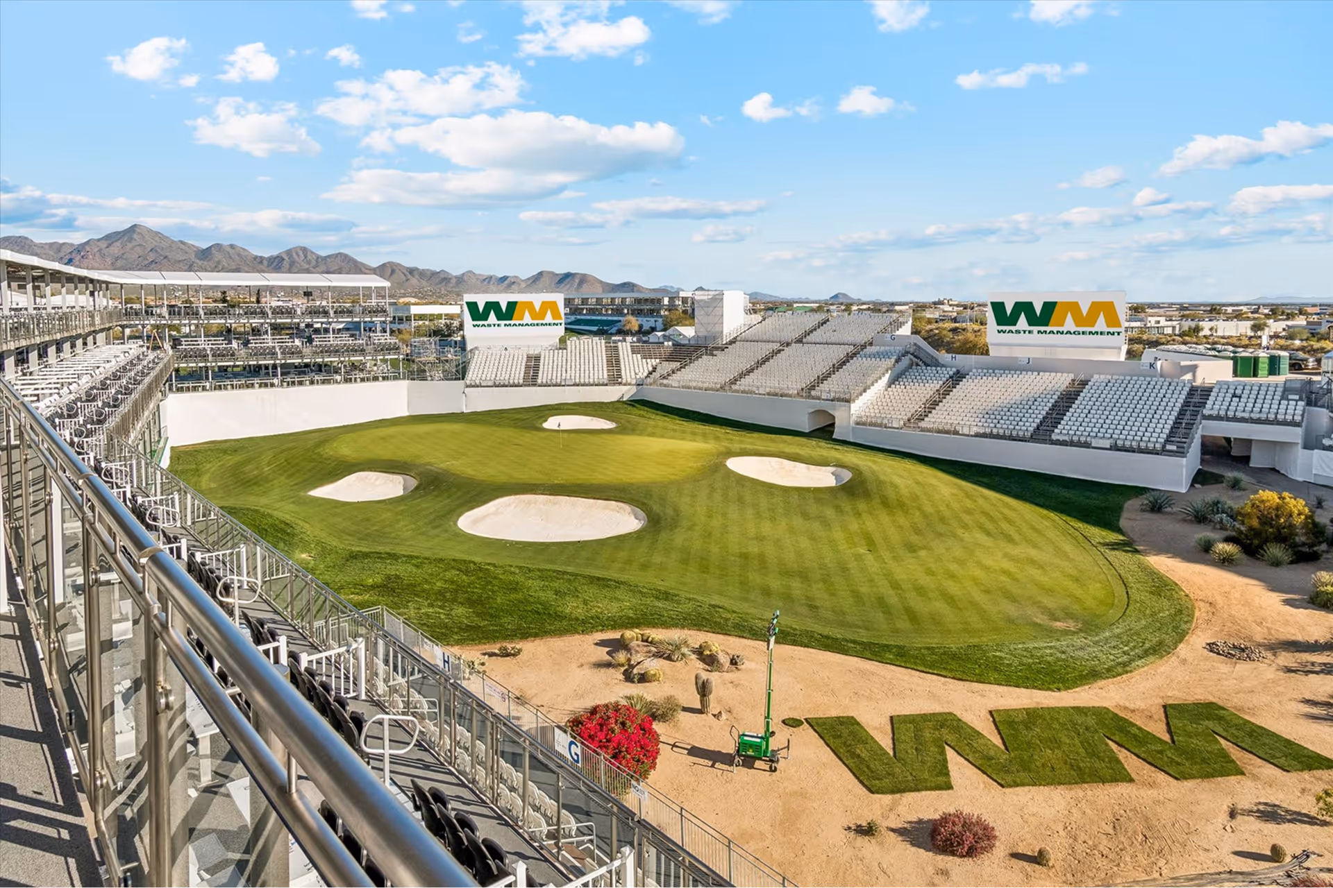 Golf course green surrounded by spectator stands with Waste Management logos and desert landscaping in the foreground.