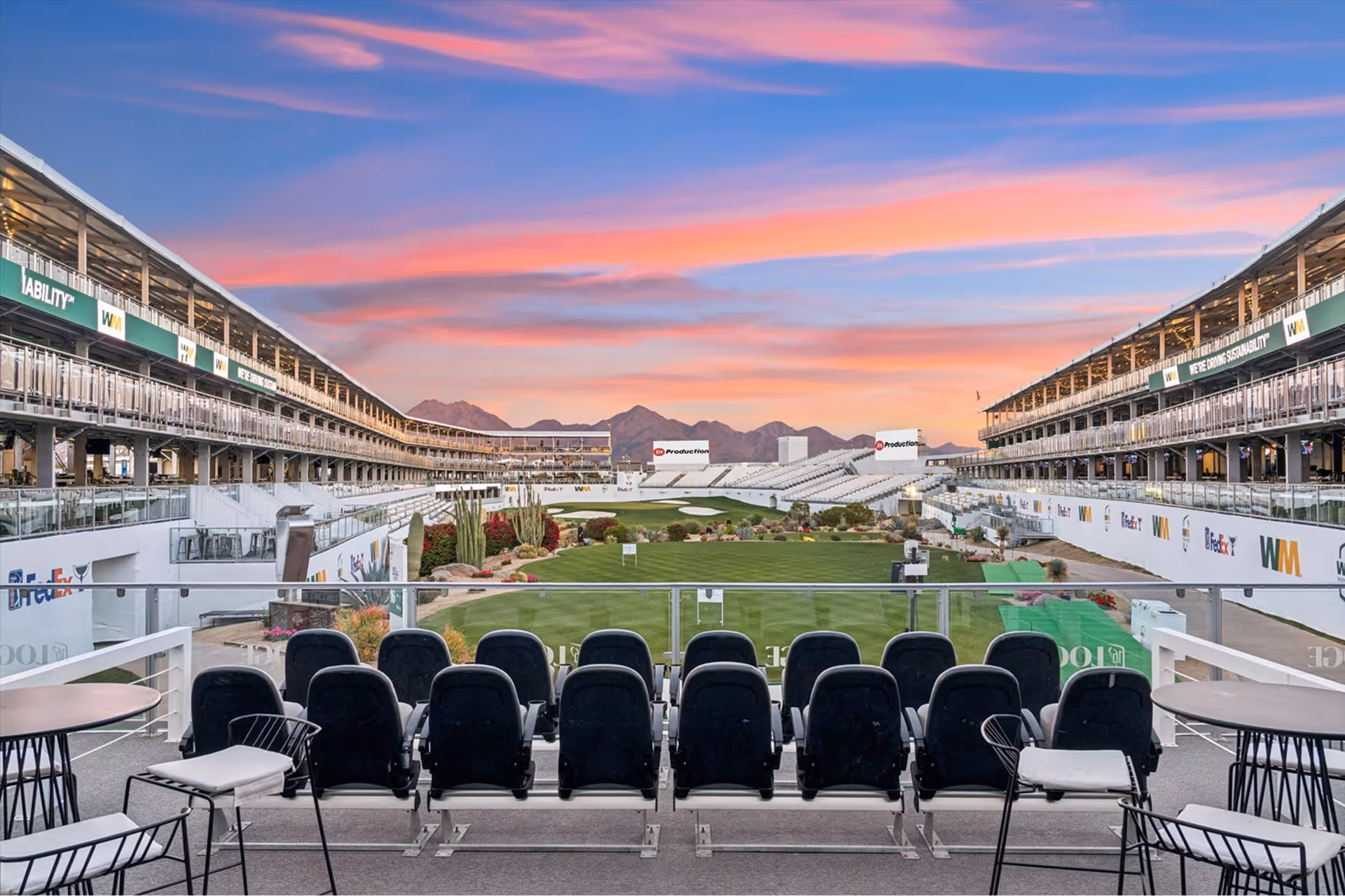 Golf stadium seating overlooking a green golf course with mountains in the background at sunset.