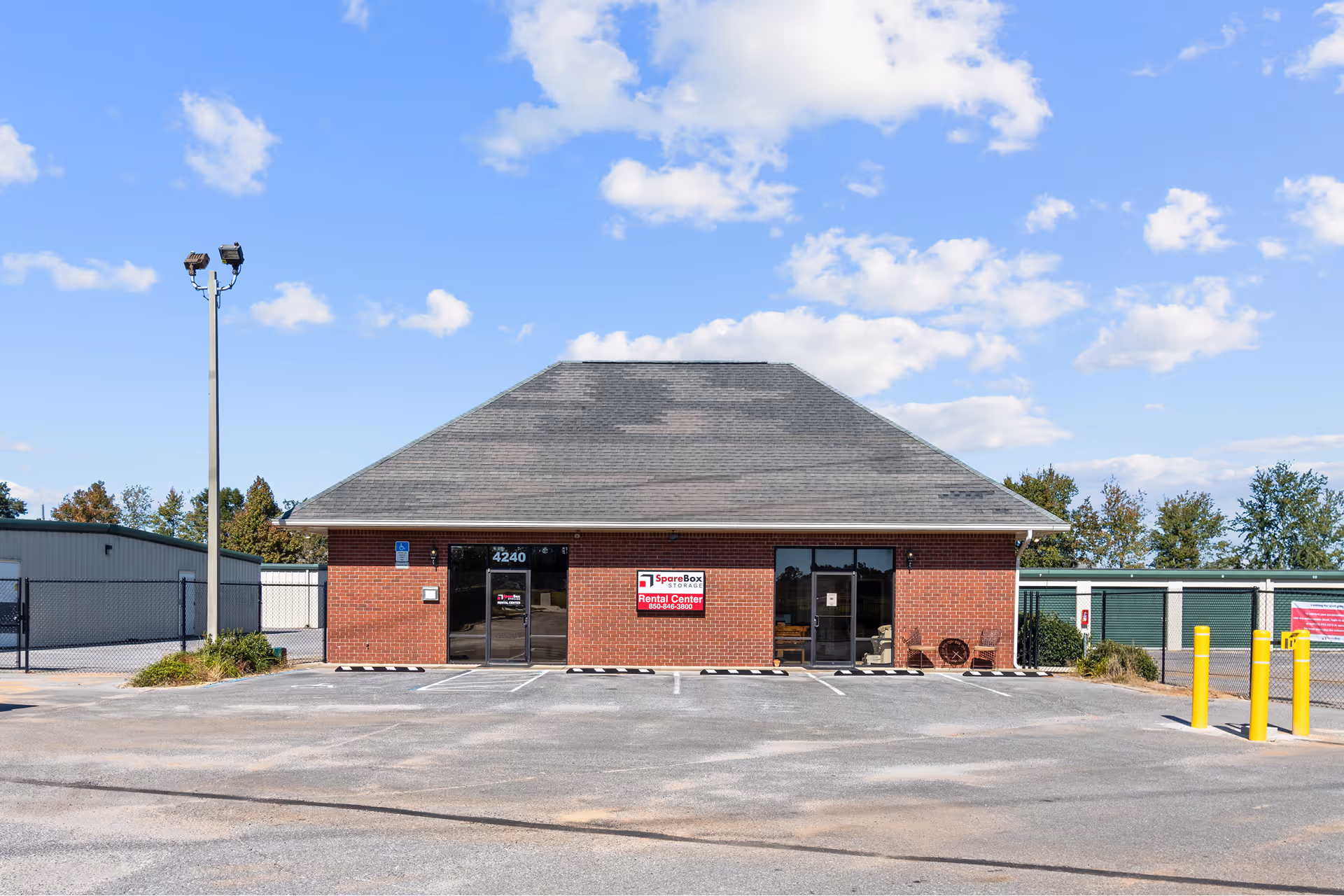 Brick building with two glass doors labeled 'Rental Center' and 'SpareBox Storage' sign under clear blue sky.