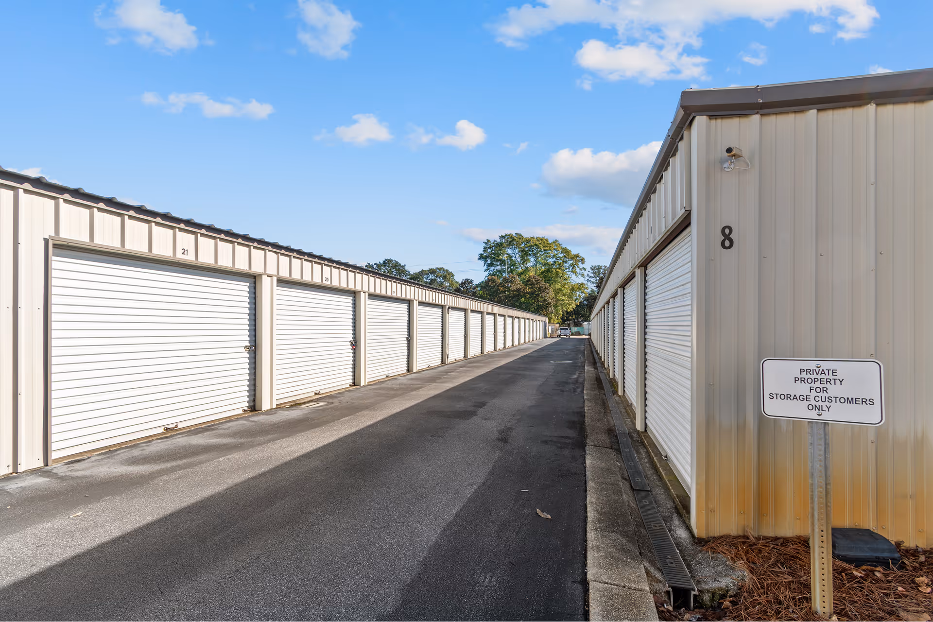 Outdoor self-storage facility with rows of closed white roll-up doors under a blue sky with scattered clouds.