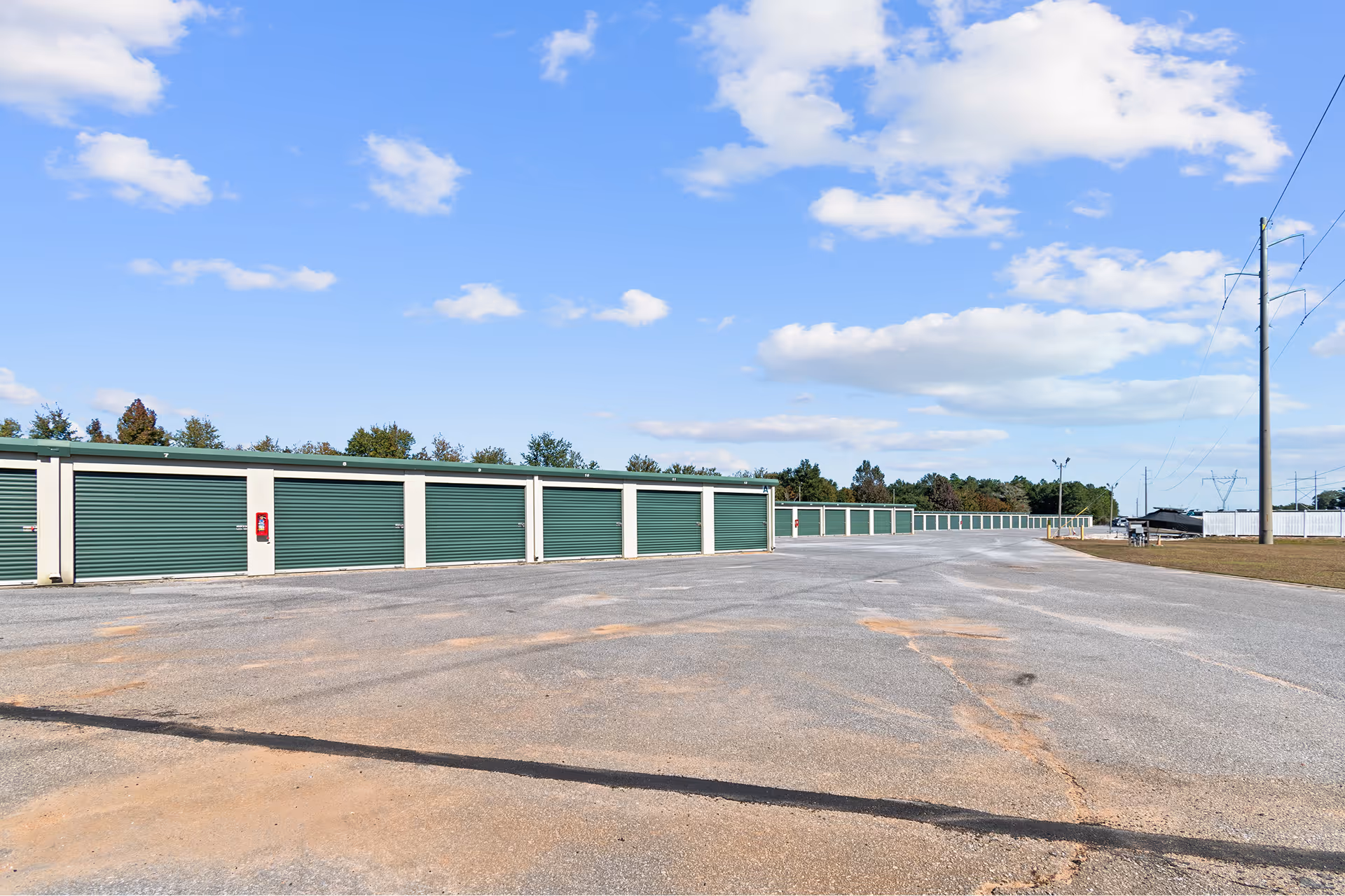 Row of green storage unit doors at an outdoor storage facility under a partly cloudy blue sky.