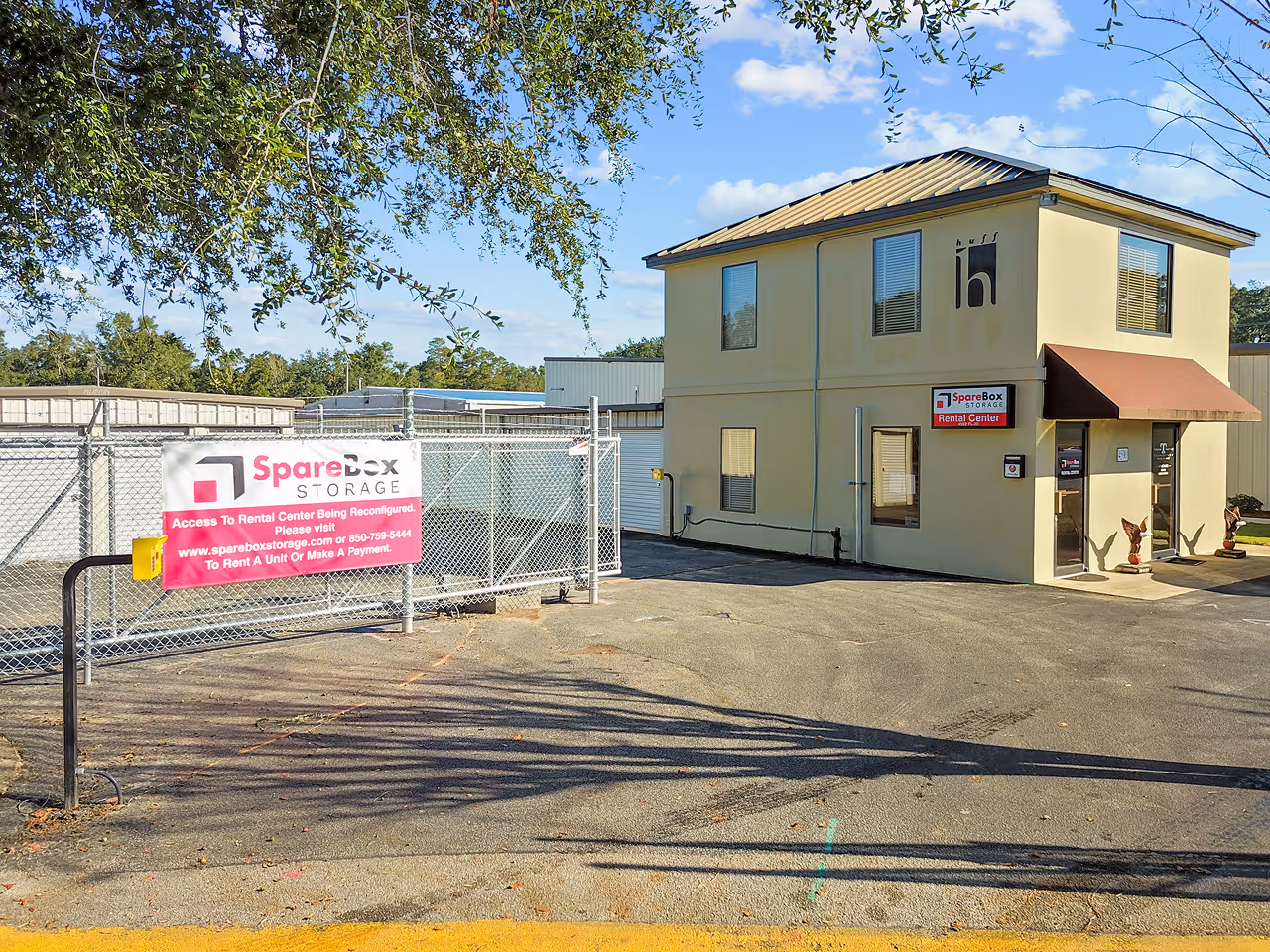 Entrance to SpareBox Storage Rental Center with fenced gate and beige two-story office building under a sunny sky.