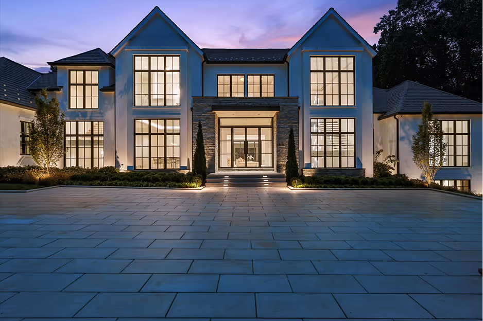 Large modern two-story house with tall windows and illuminated entrance at dusk.