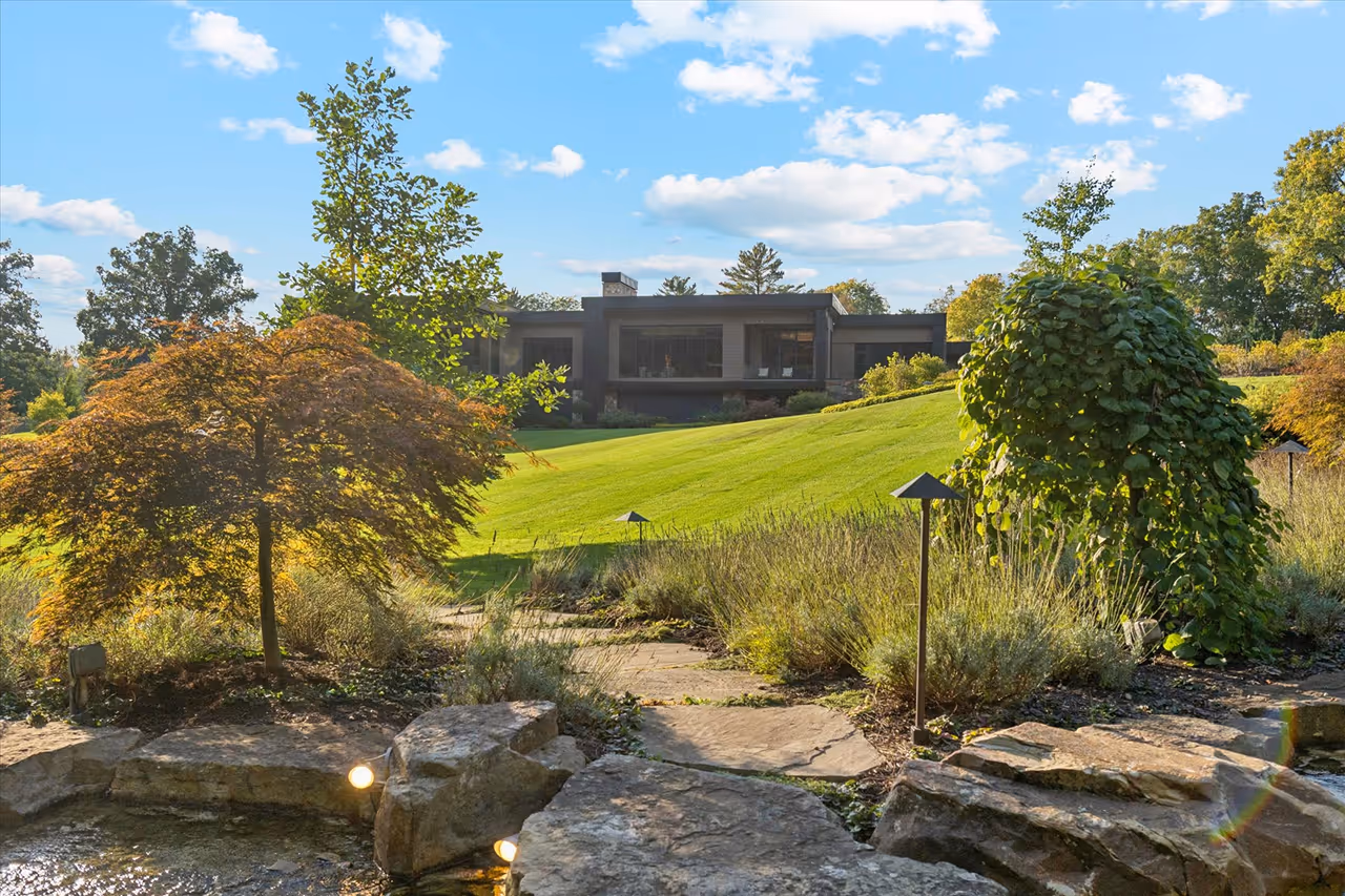 Modern house with large windows overlooking a lush green lawn, landscaped garden, and stone path with outdoor lighting.